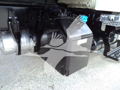 Truck undercarriage showing a plastic 5-liter coolant reservoir with blue cap mounted near frame; surrounding components include metal brackets and hoses.