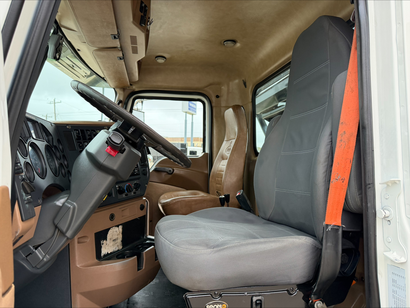 Cab interior of a 2016 Mack GU533 truck showing steering wheel, dashboard, and single gray seat with orange seat belt.
