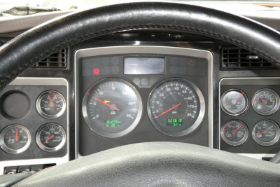 Dashboard view from a Kenworth truck cab showing gauges and steering wheel; instrument cluster includes speedometer, tachometer, and smaller gauges.