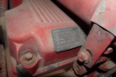 Engine data plate on red Kenworth T660 indicating engine and model details; visible screws, hoses, and brackets around plate.