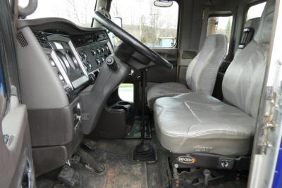 Interior of a 2014 Kenworth T660 conventional daycab showing driver seat and dashboard with steering wheel, gear shifted, and pedals visible.