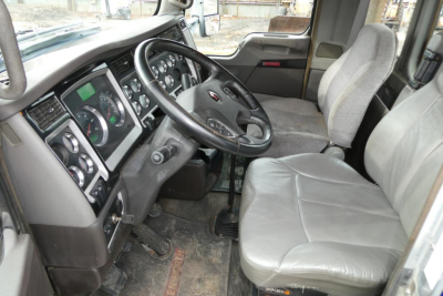 Kenworth T660 cab interior showing steering wheel, dashboard gauges, and gray seats.