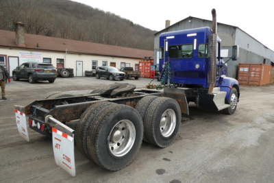 Kenworth T660 axle and cab rear showing triple axle wheel setup and blue tractor with fifth wheel plate.