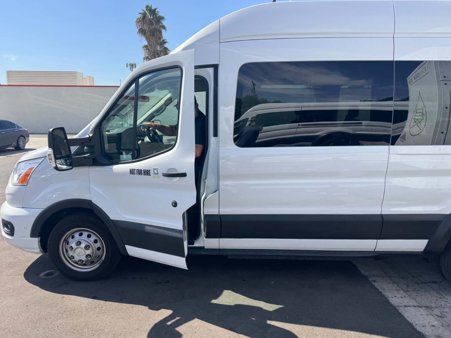 Ford Transit 350 HD XLT passenger van side view showing open front passenger door, slate gray trim, wheel hub, and VIN plate area with text 'New York' style decals.