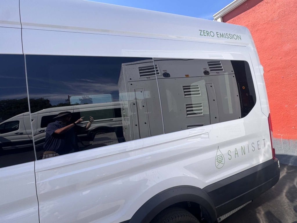 Ford Transit 350 HD XLT van with zero emissions badge and Saniset branding on the side, rear window reflection showing equipment inside.