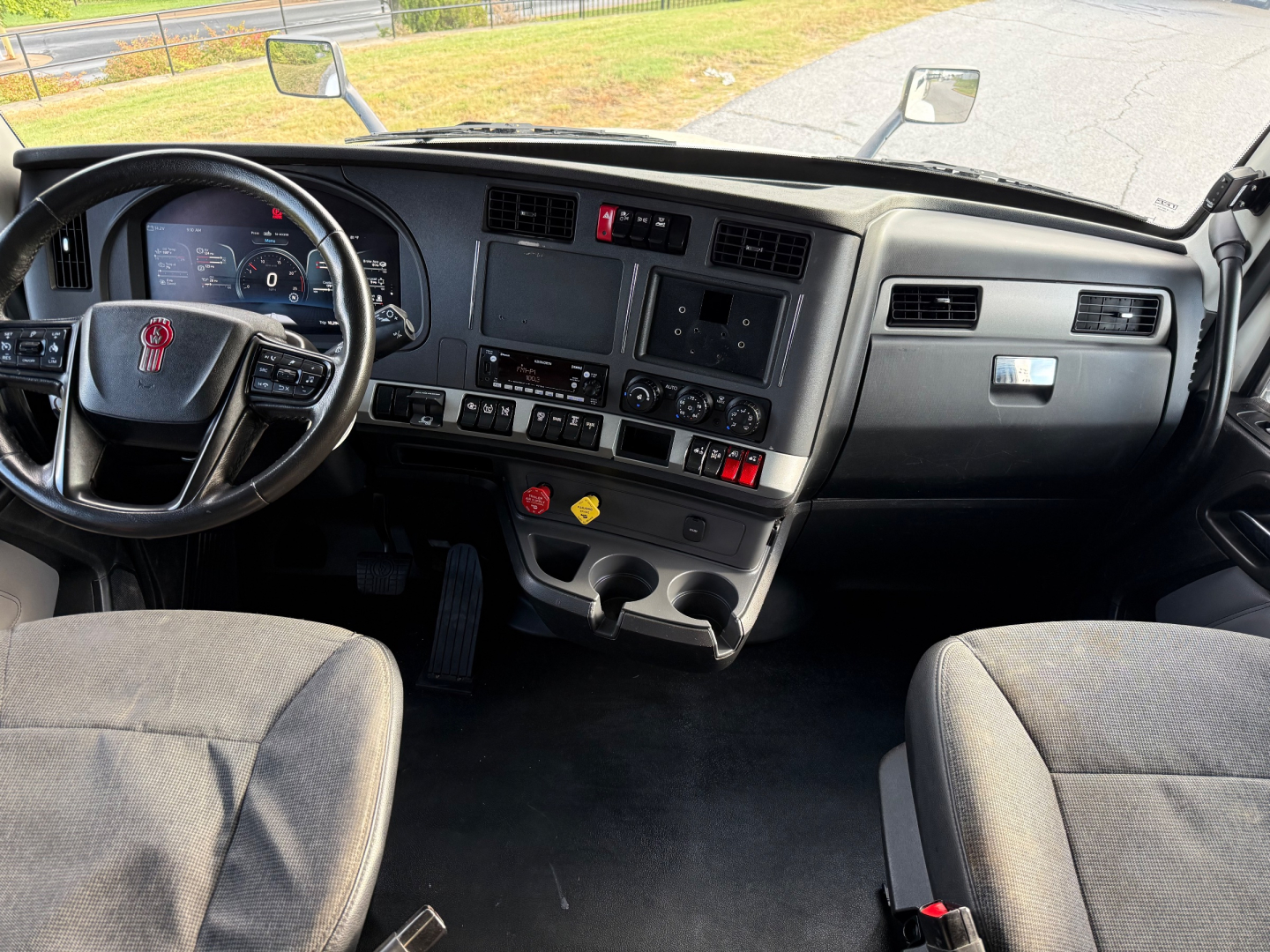 Kenworth T880S truck cab interior showing steering wheel, dash, center console, and infotainment screens with dual cup holders and controls.