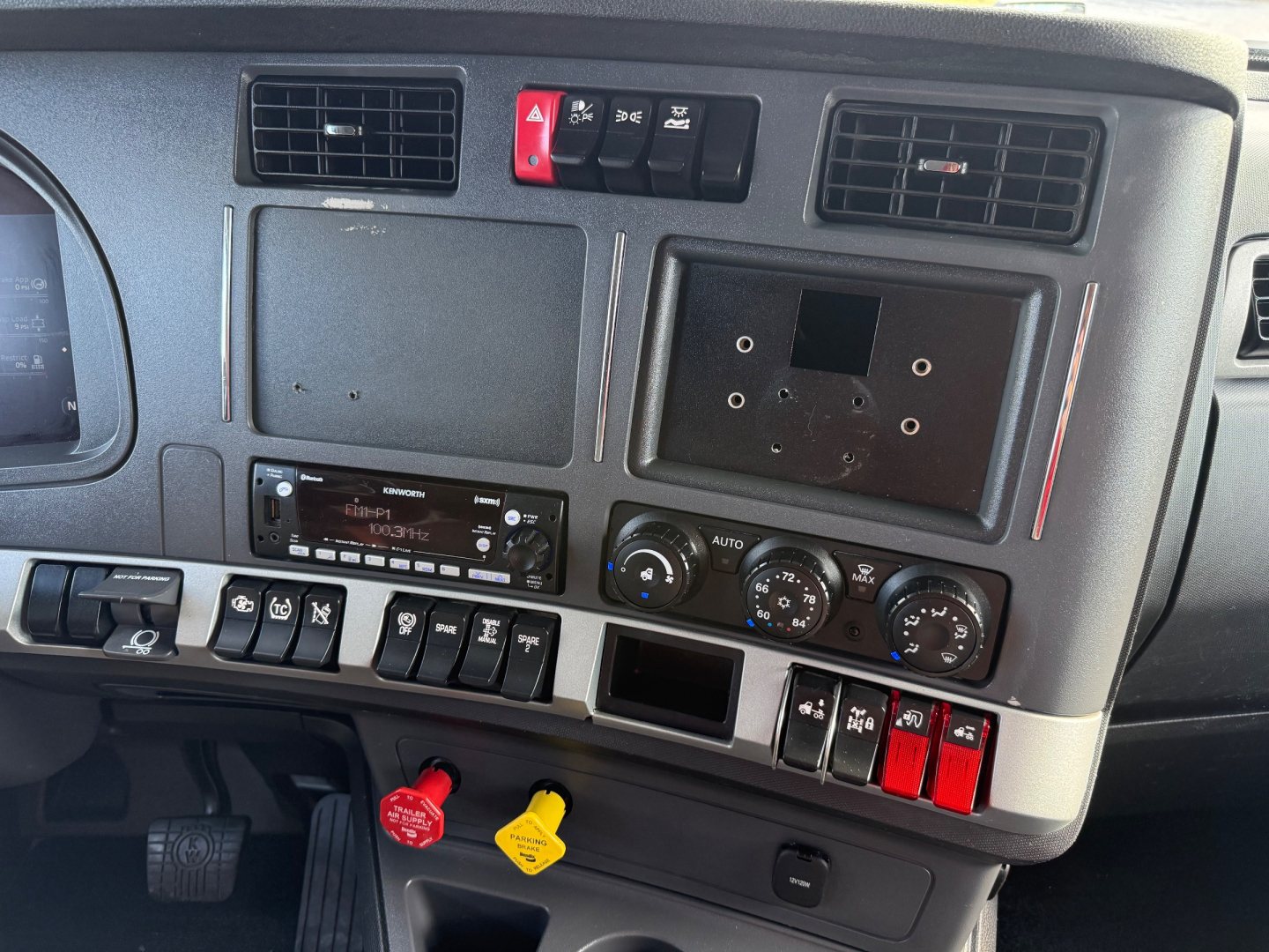 Vehicle dashboard and center console of a Kenworth T880S truck showing controls, vents, switches, and dashboard panels.