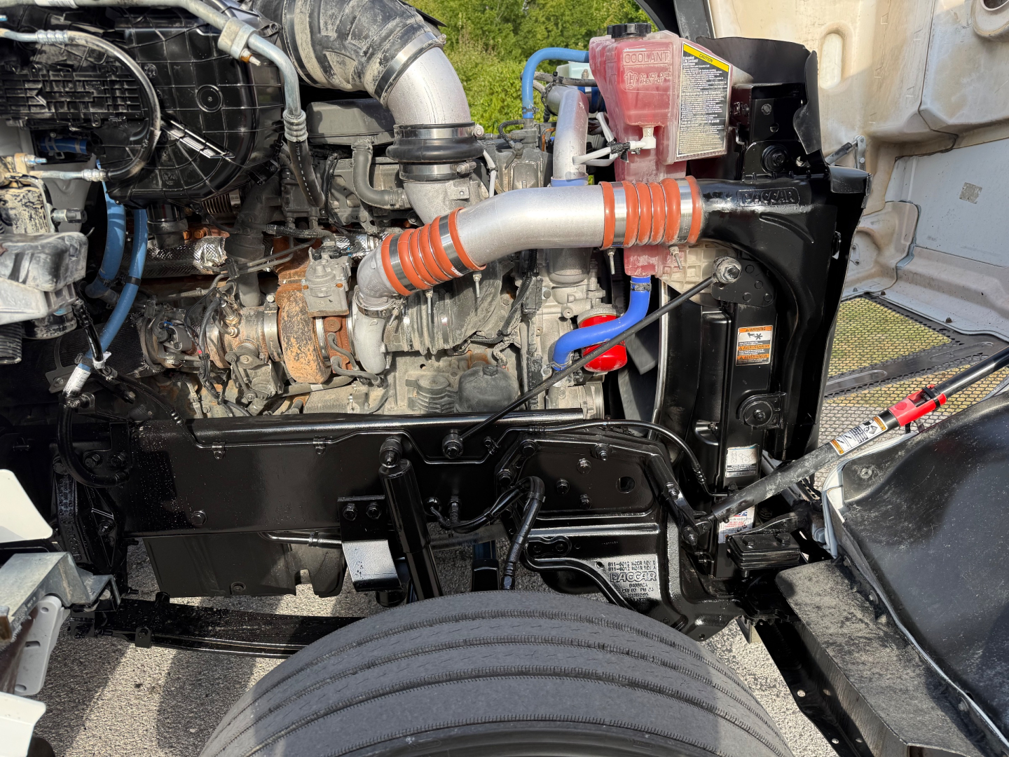 Kenworth T880S engine bay showing coolant hose, air intake, and engine components with wiring and frame visible.
