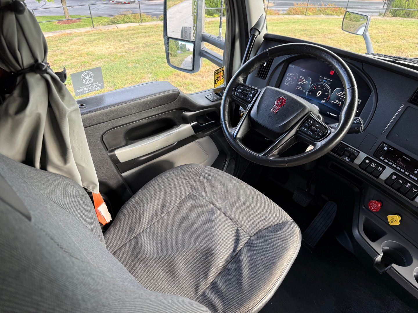Kenworth T880S truck interior showing steering wheel and dashboard with gray fabric seat and driver-side door.