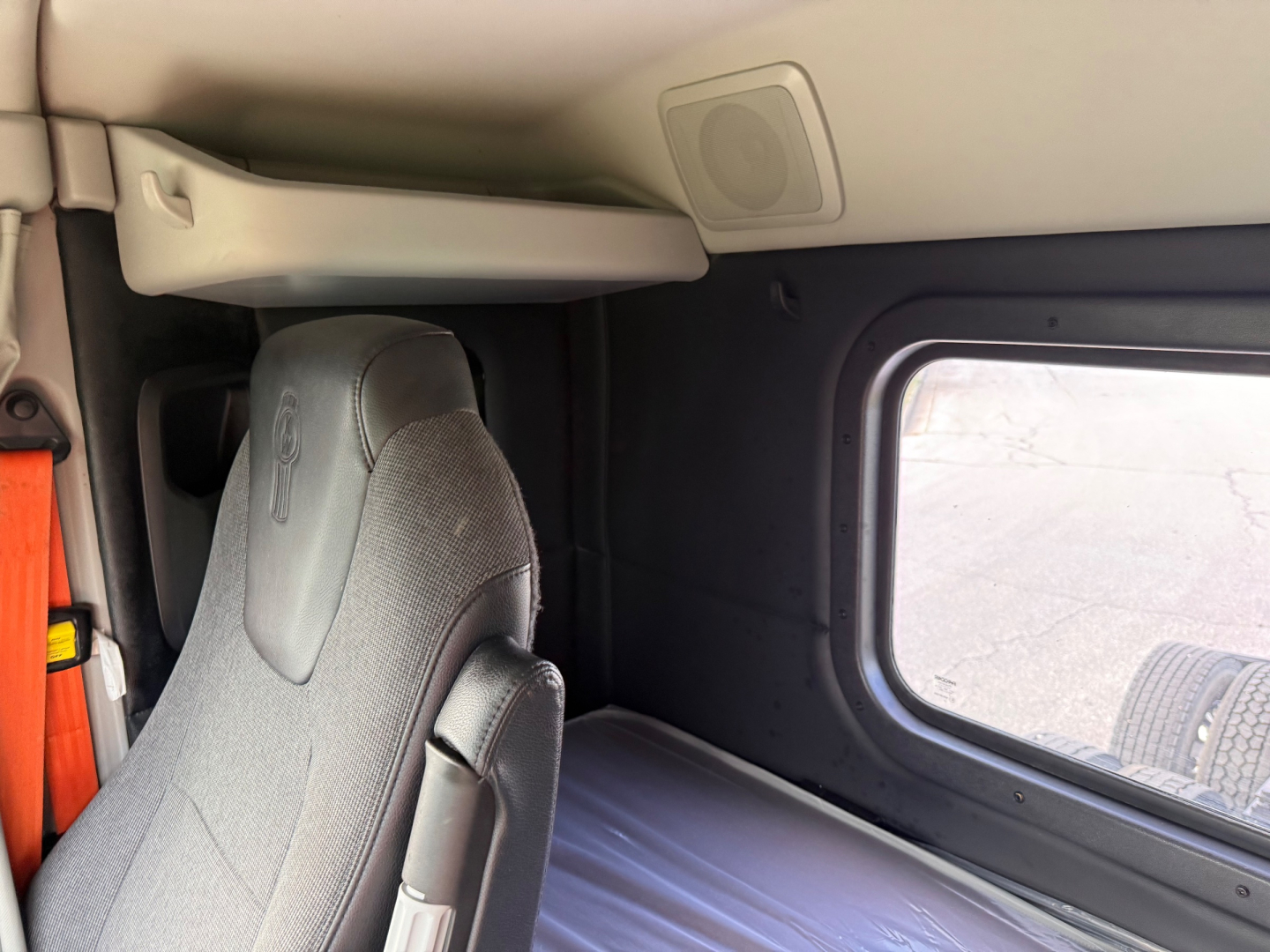 Cab interior of a Kenworth T880S showing sleeper area with fabric seat, window, and overhead storage panel.