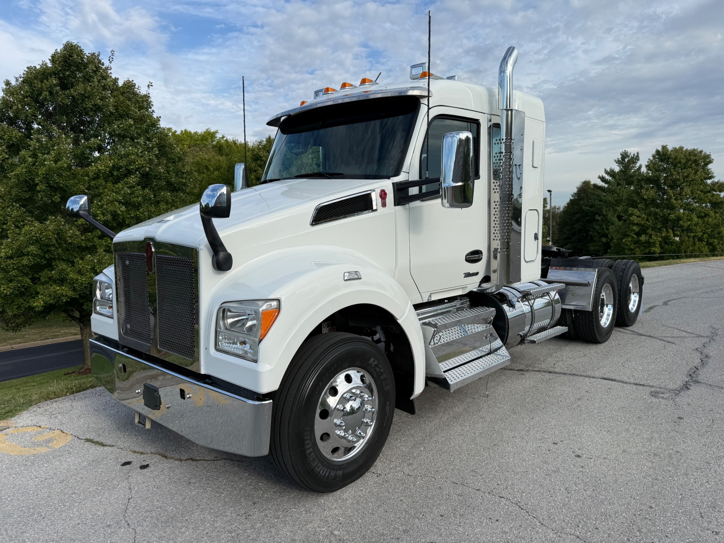 Kenworth T880S tractor cab in white, front-left angle, with chrome bumper, dual exhaust stacks, and sleeper cab; visible fuel tanks and steps; truck sits on a paved lot.