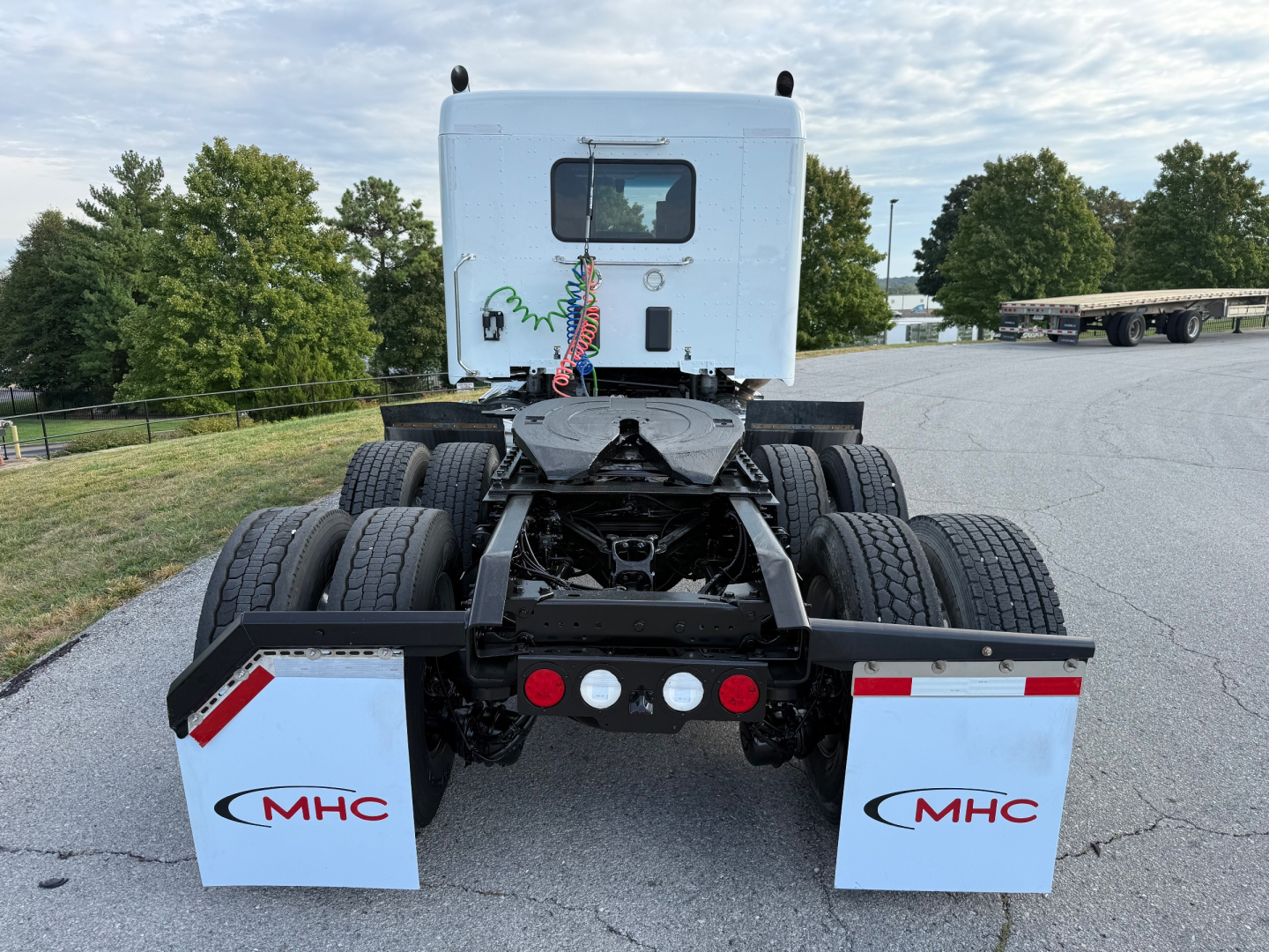 Kenworth T880S truck chassis rear view showing fifth wheel, dual rear axles, mud flaps with MHC logo, and rear lights.