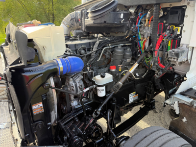 Kenworth T880S engine bay with visible hoses, wiring, coolant reservoir, air intake, and various components; stickers and labels partially legible.