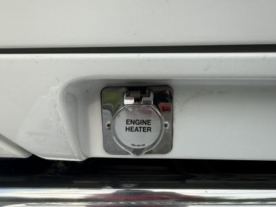 Engine heater cap on front bumper of a Kenworth T880S with white paint and chrome cover.