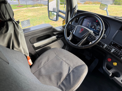 Kenworth T880S truck interior showing steering wheel and dashboard with gray fabric seat and driver-side door.
