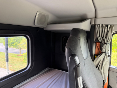 Kenworth truck interior ceiling area with sleeper compartment, small speaker and window side visible; partial seat and curtain in view.