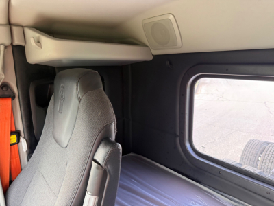 Cab interior of a Kenworth T880S showing sleeper area with fabric seat, window, and overhead storage panel.