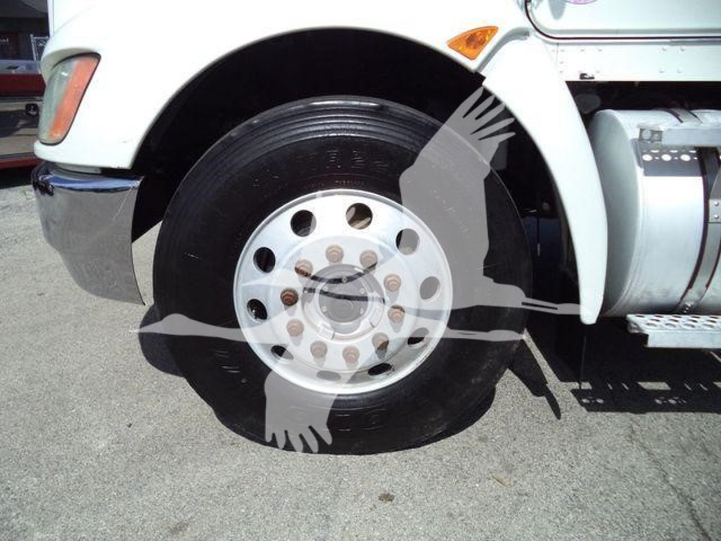 Truck front wheel showing steel wheel with hubcap and partial fender of a white Kenworth T270 cab over engine truck.