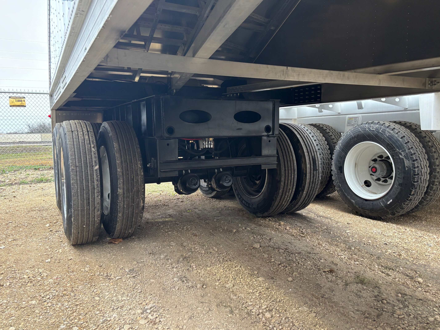 Hopper trailer undercarriage showing dual axle suspension and aluminum frame with tires and landing gear in view.