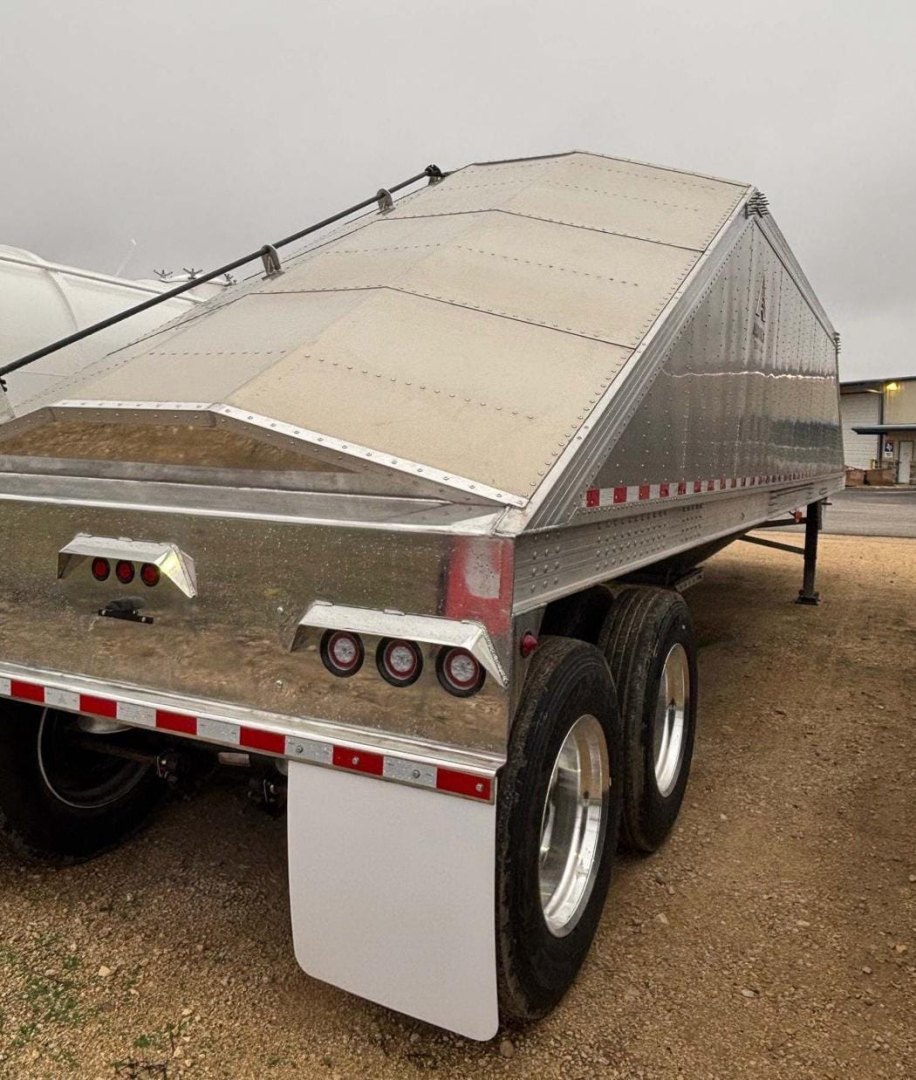 Trailer rear/side view showing aluminum sand/grain hopper trailer with diamond plate sides, dual rear axles, white mud flaps, and taillights.