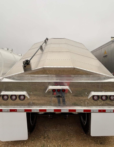 Aluminum hopper trailer rear view showing grain/sand hopper with raised cover and dual axles, taillights, and reflective striping.