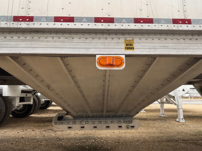 Aluminum hopper trailer underside showing tail lighting and support frame with warning sticker; wide turn sign and riveted seams.