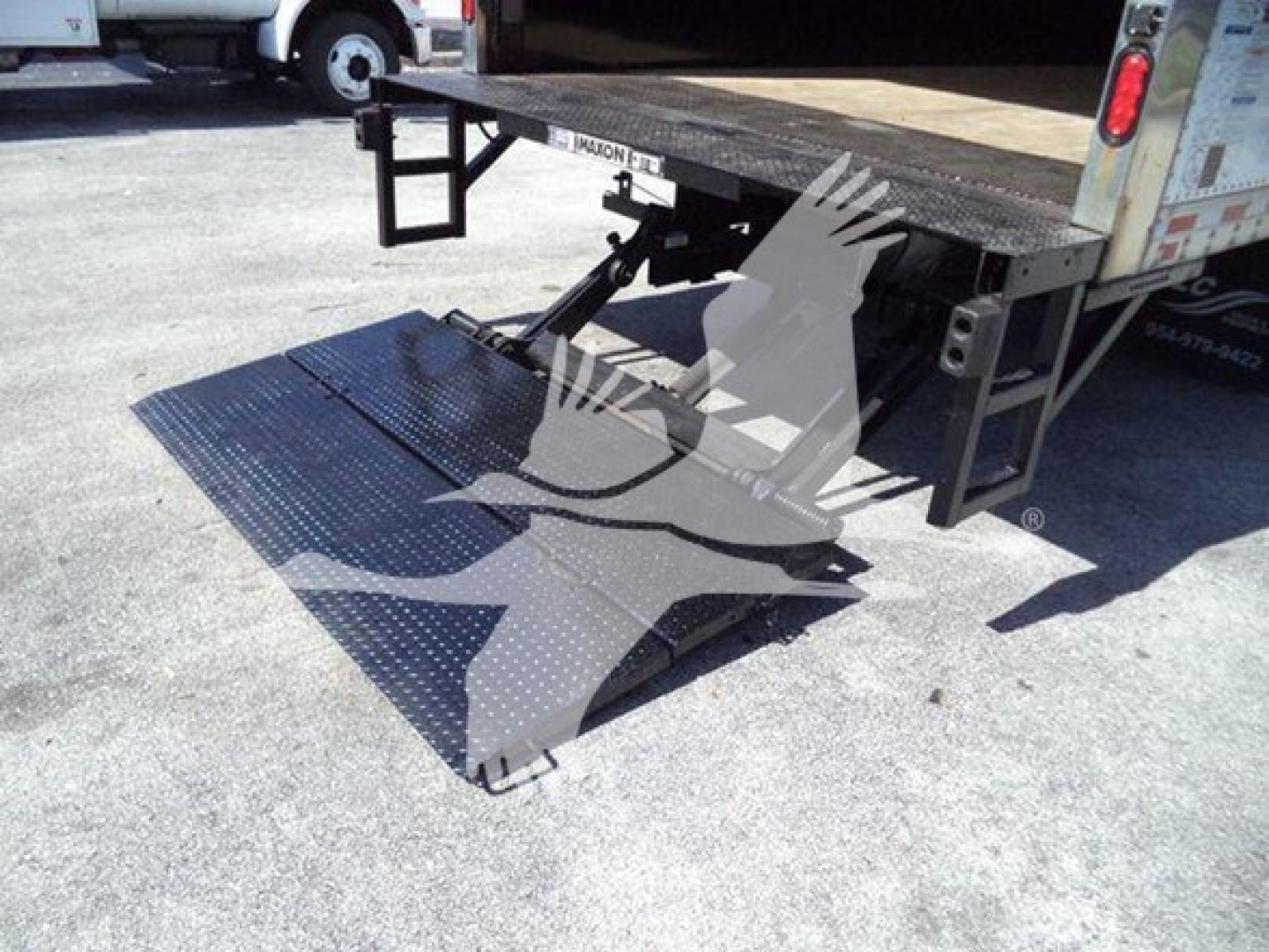 Isuzu NPR truck with a side-mounted hydraulic lift/ ramp in a loading platform, showing perforated metal ramp extended from truck bed