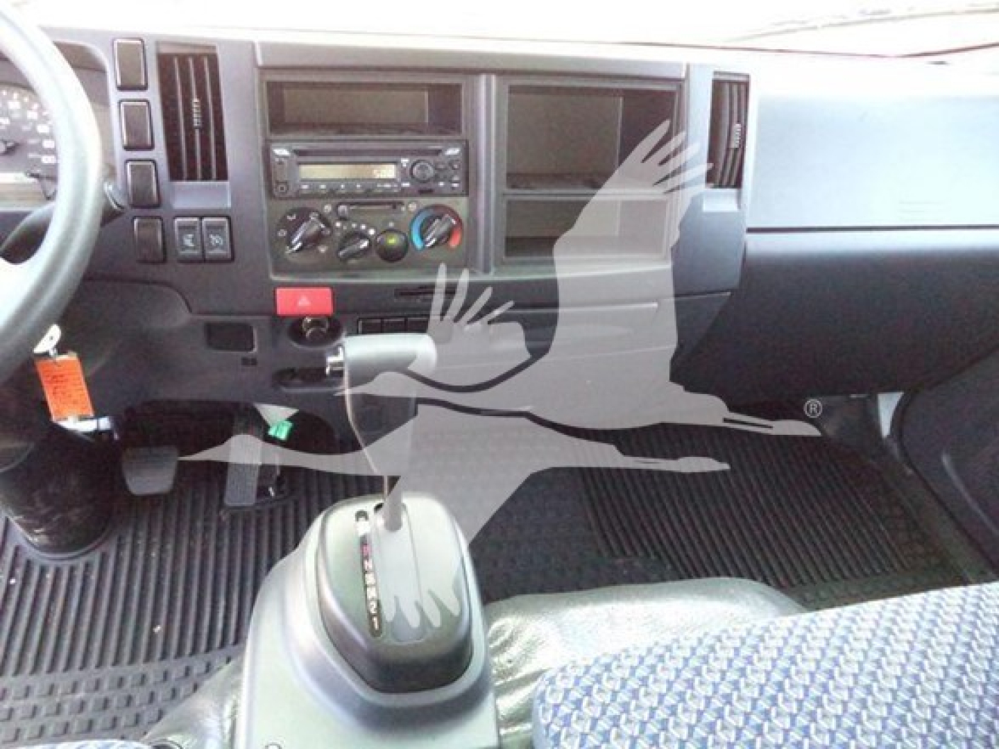 Isuzu NPR interior dashboard and gear selector visible; dash with radio, climate controls, and storage compartments; manual shifter is present.