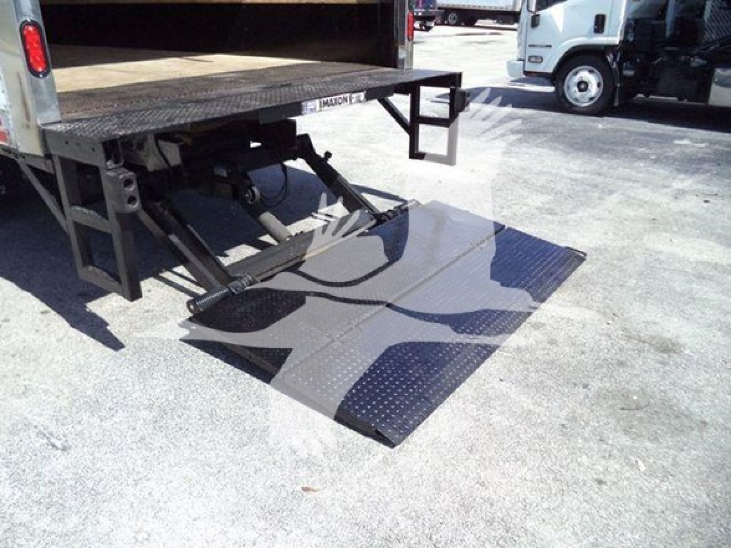 Isuzu NPR truck rear with liftgate in raised position and lowered platform showing hydraulic mechanism and ramp panels.