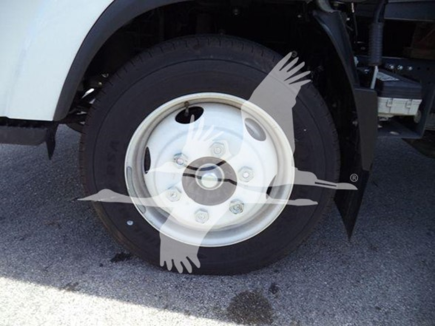 Isuzu NPR wheel well and tire visible; no legible model text on tire; wheel is white steel with lug nuts; surrounding components partially visible