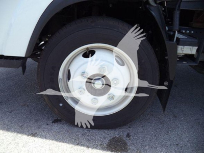 Isuzu NPR wheel well and tire visible; no legible model text on tire; wheel is white steel with lug nuts; surrounding components partially visible