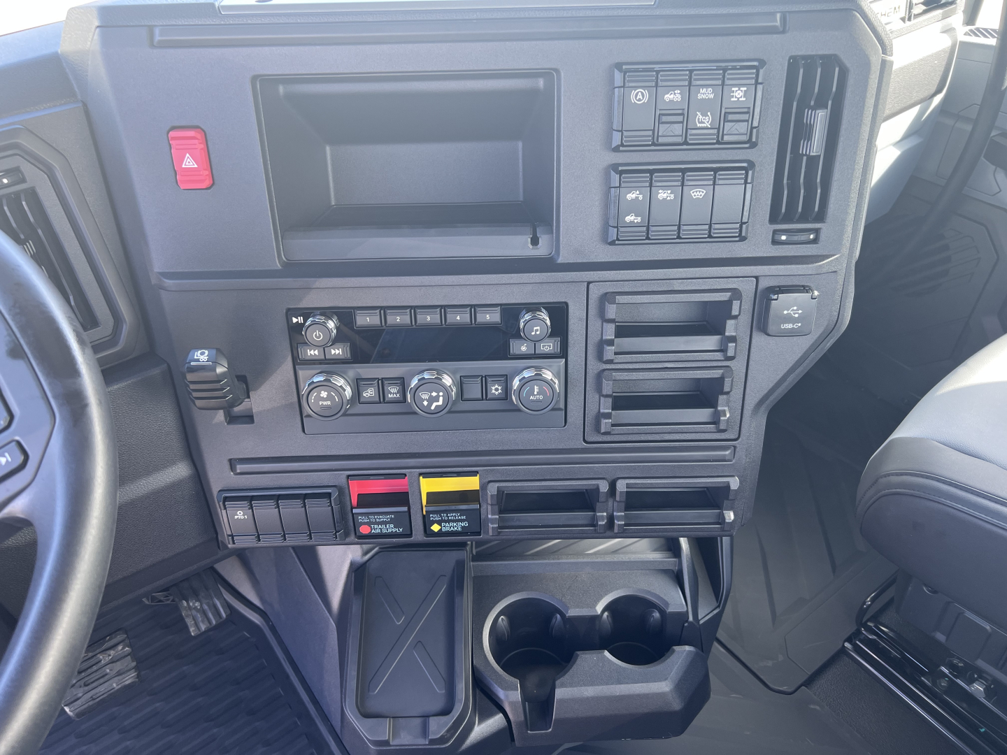 Dashboard of a Mack AN64T truck showing controls, climate dials, cup holders, and storage compartments, with various switches and an empty radio area.