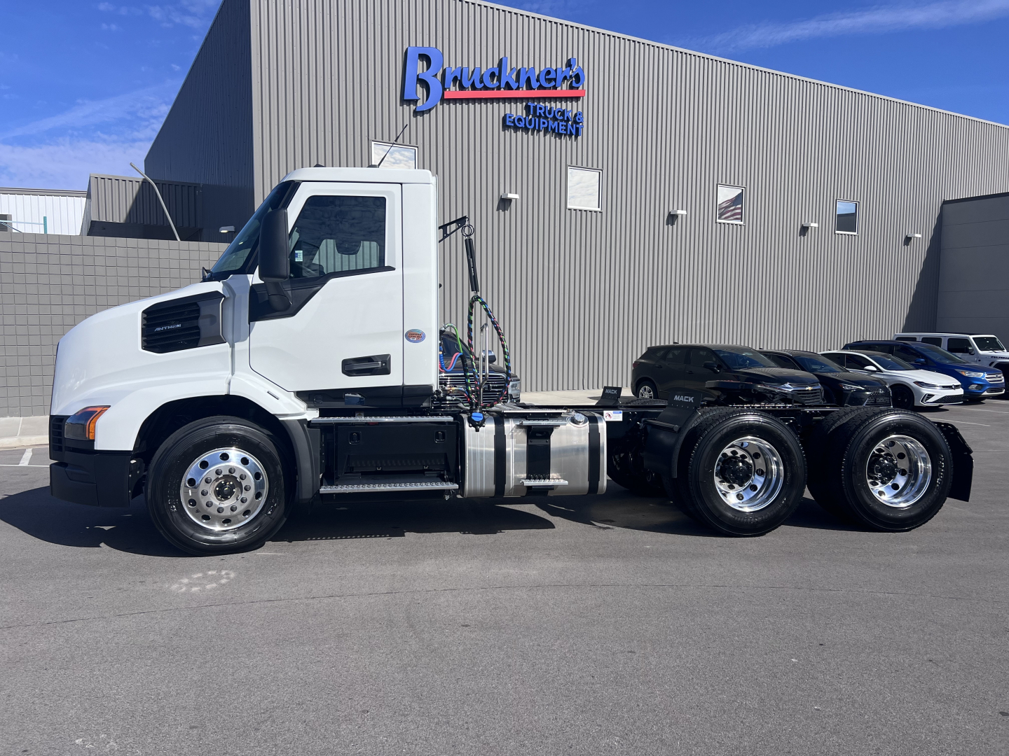 Truck chassis showing 2027 Mack AN64T daycab tractor with white cab and dual rear axles; VIN 1M1A23GY4VM101991 on the listing with Bruckner dealership in background.