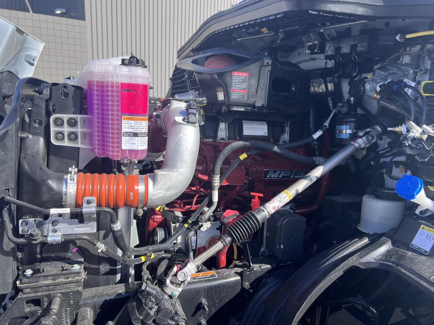 Truck engine bay showing pink DEF/ coolant reservoir, hoses, and engine components with various labels.