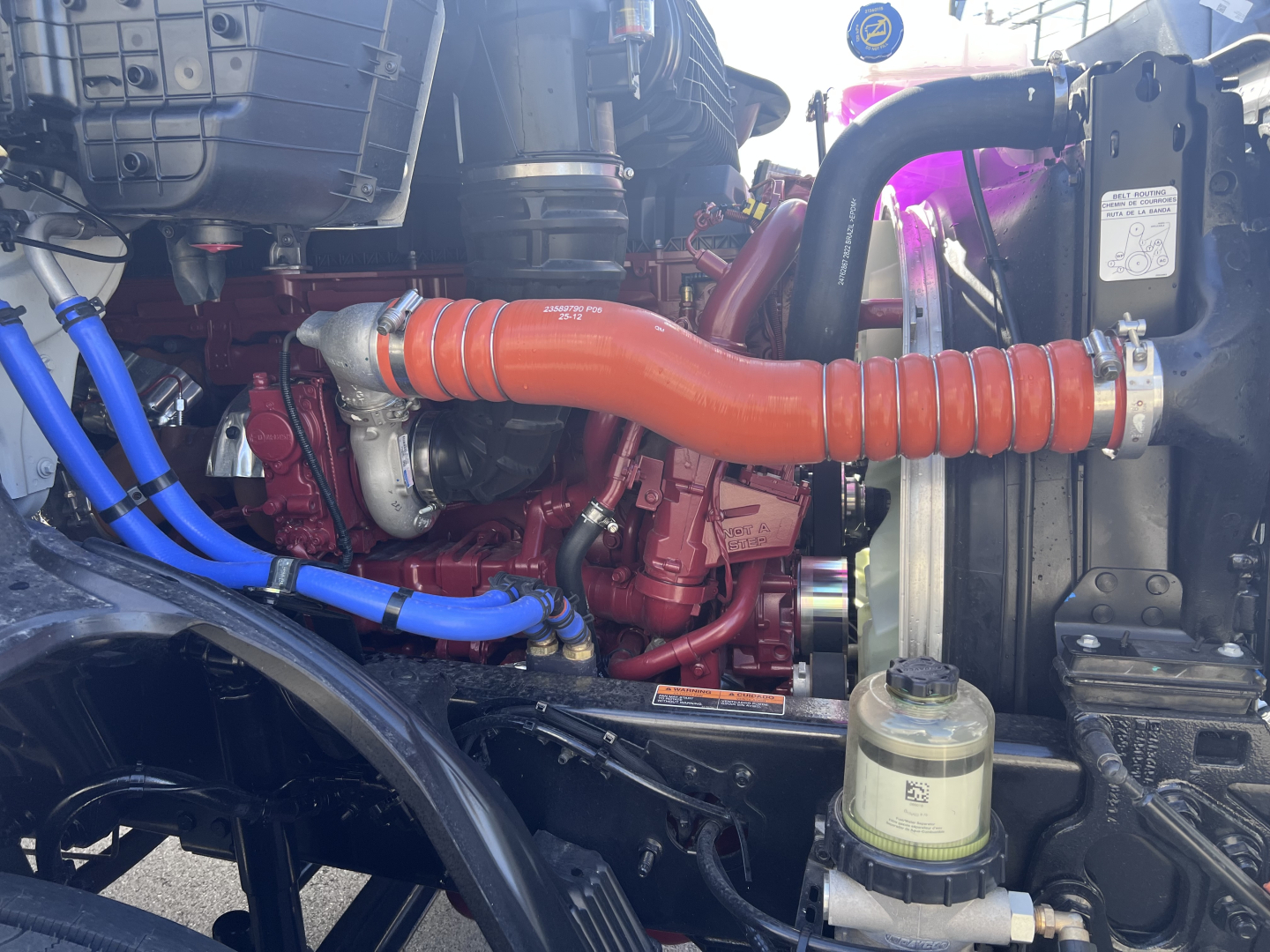 Mack AN64T engine bay showing bright orange spiral air intake hose and red engine block with blue and black hoses, coolant reservoir visible, radiator area.