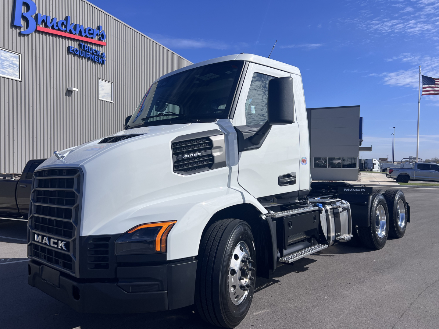 Mack AN64T truck in white cab showing side view and front grille with black bumper and dual rear axles at dealership.