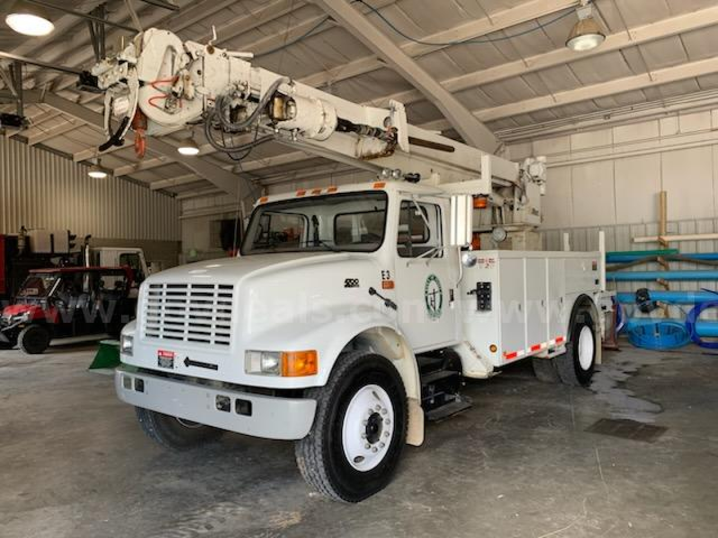 International 4700 bucket truck in a warehouse with boom arm raised, front view showing white cab and utility body