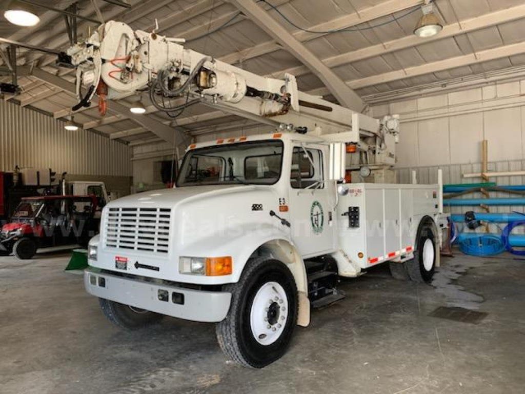 International 4700 bucket truck in a warehouse with boom arm raised, front view showing white cab and utility body