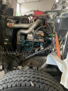 Truck engine bay showing diesel engine with intake pipes, hoses, wiring, and surrounding components in a digger-derrick setup.