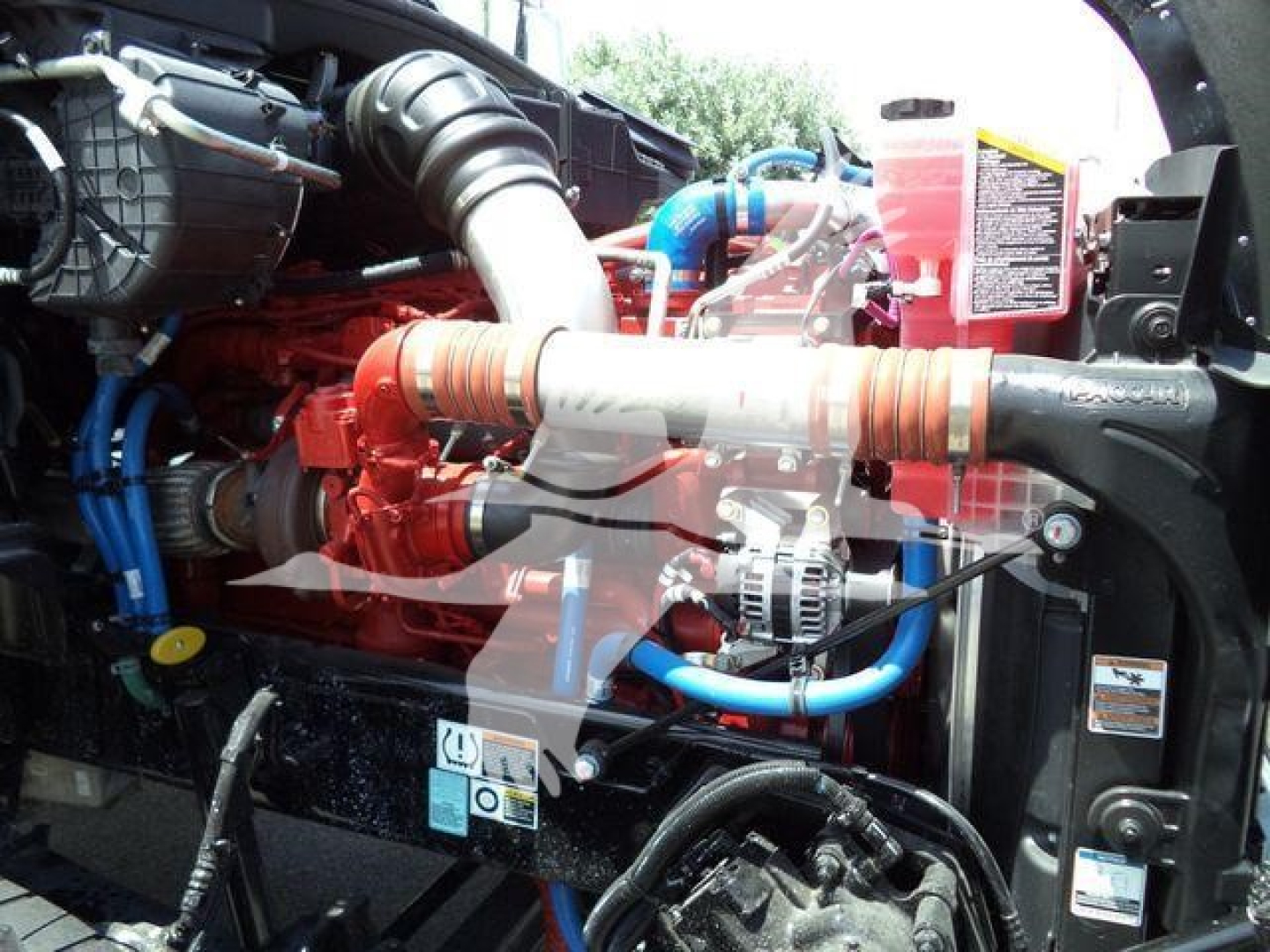 Kenworth T880 engine bay showing coolant reservoir, red engine, blue hoses, and alternator.