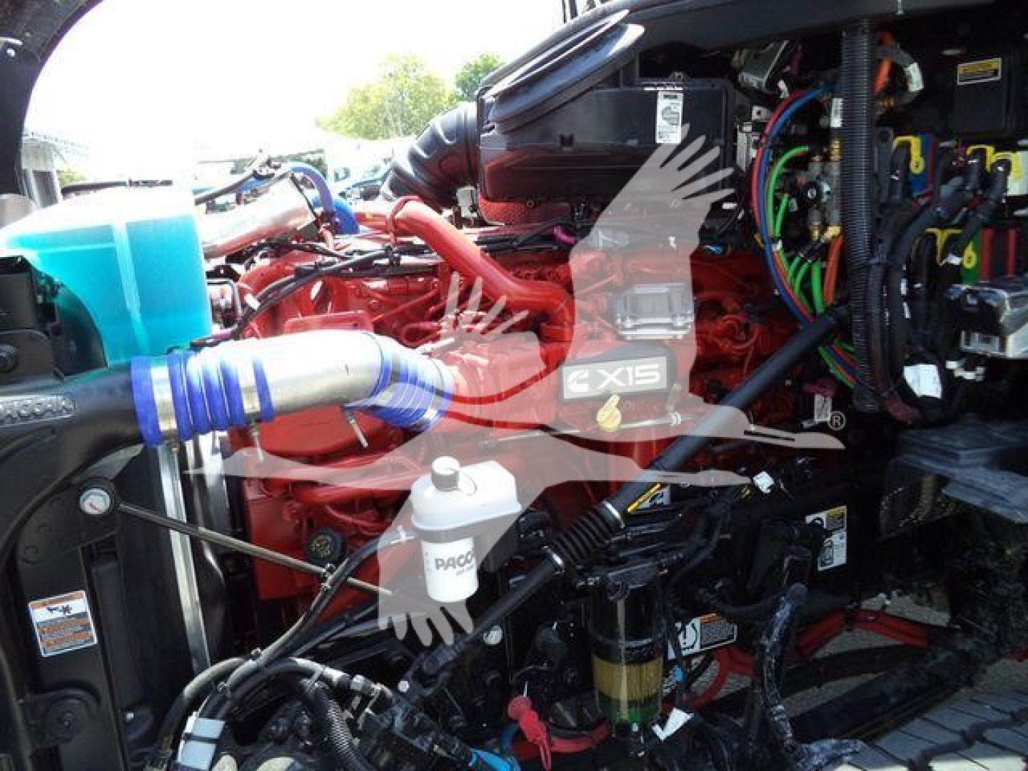 Kenworth T880 engine bay showing X15 emblem on engine cover and various hoses, wiring, and fluid reservoirs in the open hood area.
