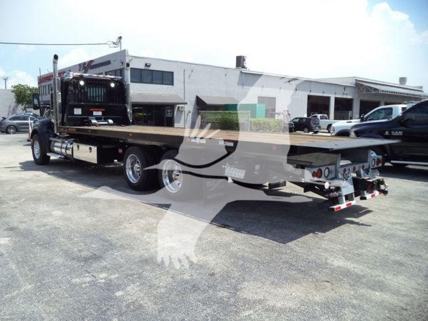 Kenworth T880 rollback truck in a parking lot, flatbed with loading ramps and rear lighting, side view highlighting chassis and wheels.