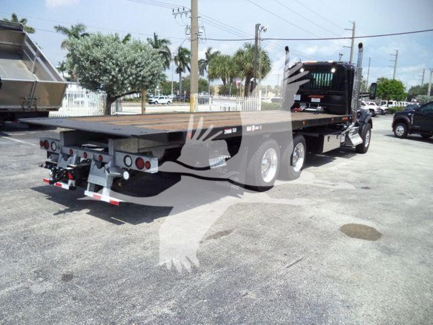 Kenworth T880 rollback truck rear/side view showing flatbed with dual rear axles and rear bumper; side cab visible in distance; tail lights and platform controls.