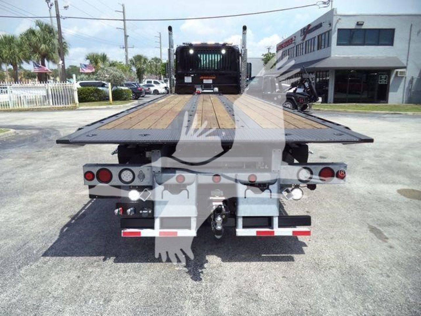 Flatbed tow truck rear view showing wood deck, taillights, and towing equipment on a Kenworth T880 rollback.