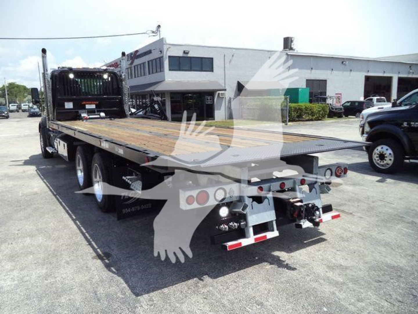 Kenworth T880 rollback truck in an outdoor lot, rear view showing flatbed with tail lights and towing equipment.