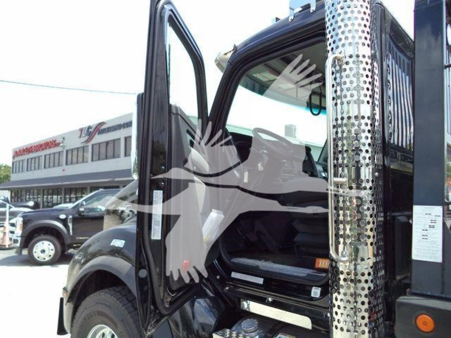 Truck cab interior and door frame of a new Kenworth T880 with open door, chrome exhaust stack, and surrounding dealership lot.