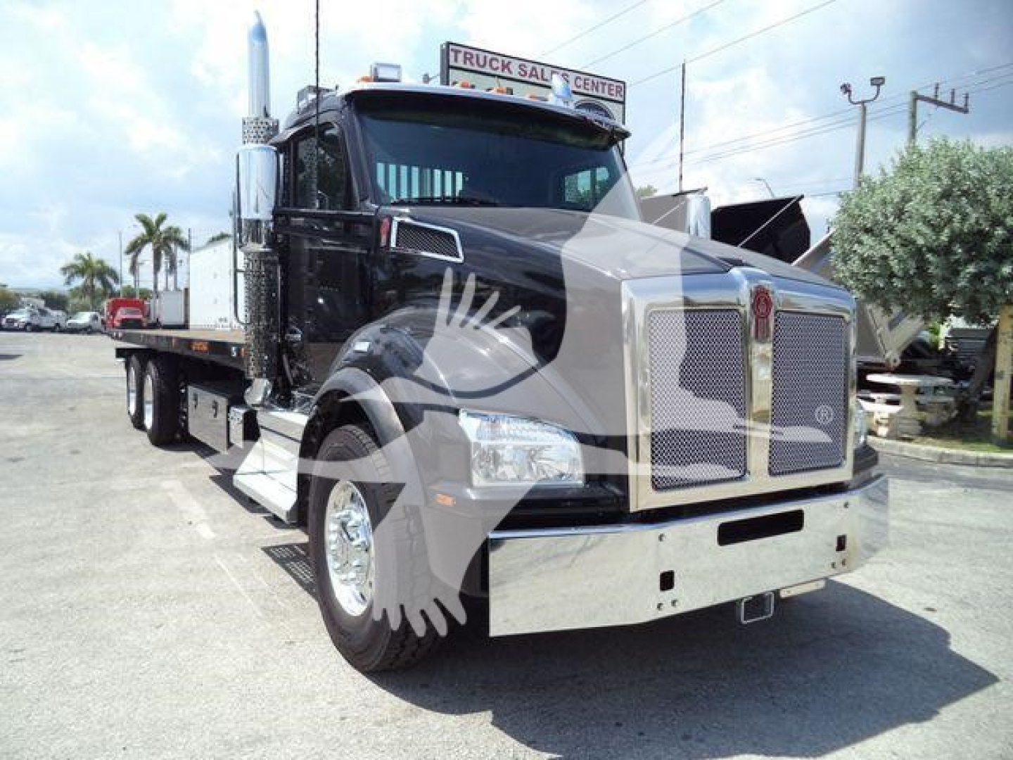 Kenworth T880 rollback truck in black, front three-quarter view showing chrome grille, large bumper, and flatbed with load.