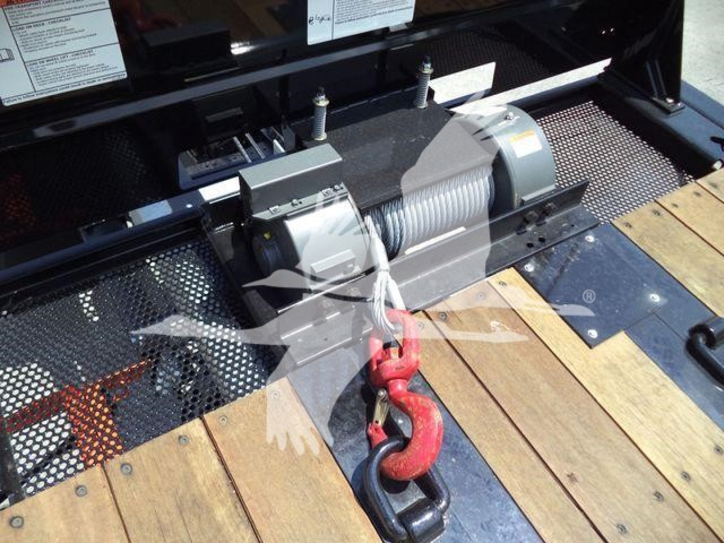 Winch assembly on a Kenworth T880 rollback truck showing electric winch drum and hook on wooden deck.