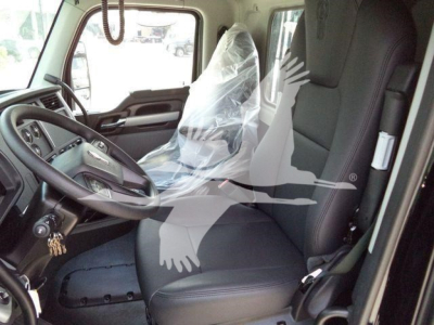 Truck cab interior of a 2026 Kenworth T880 with plastic seat coverings and steering wheel visible, dashboard area, driver seat and passenger seat.