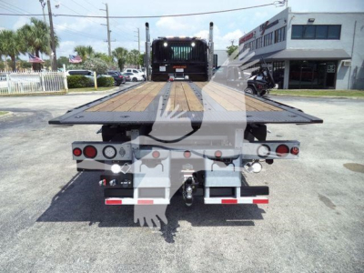 Flatbed tow truck rear view showing wood deck, taillights, and towing equipment on a Kenworth T880 rollback.
